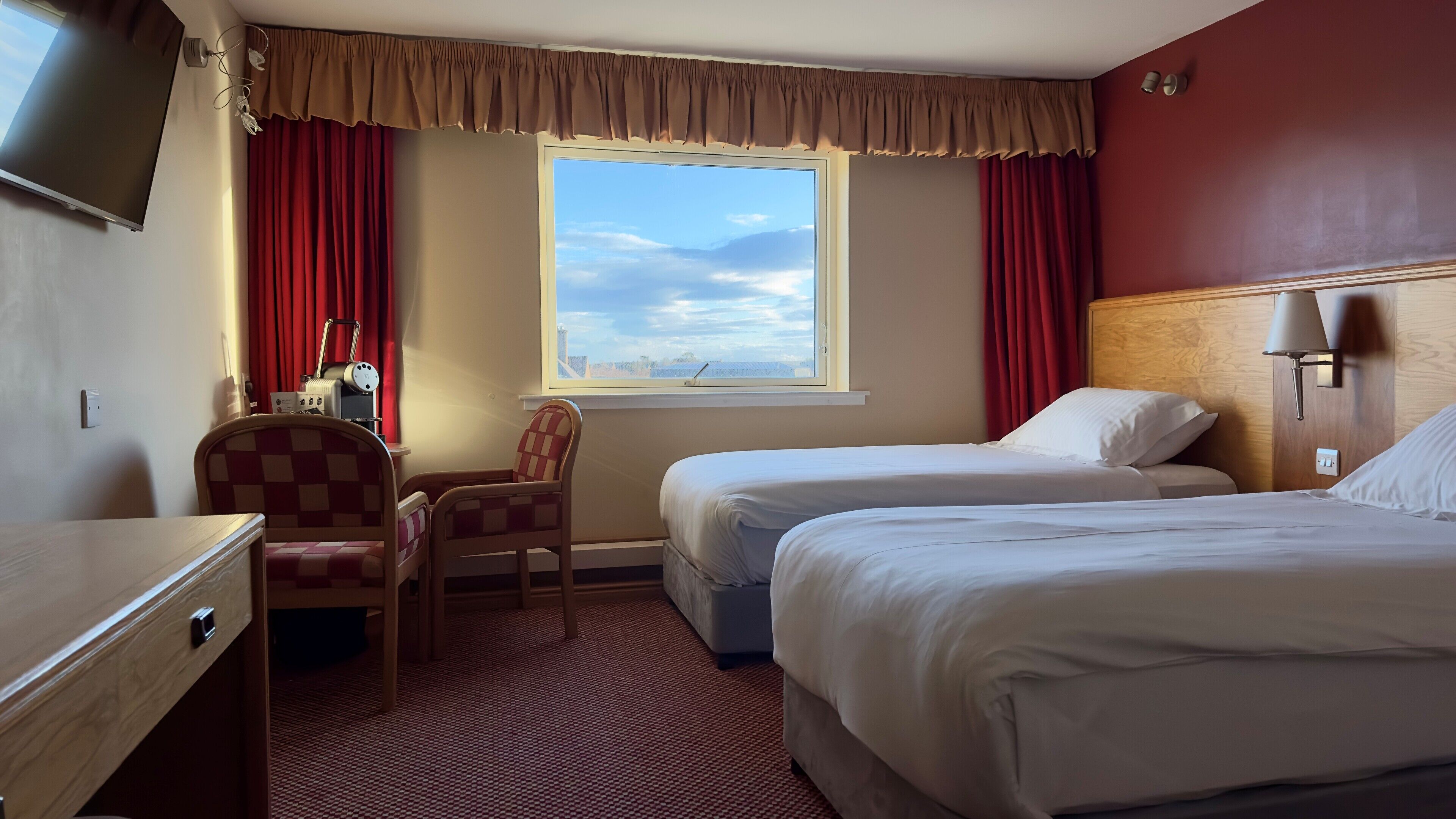 A hotel room with two beds, a desk, a chair, and a large window with a view.