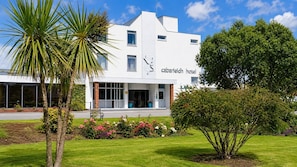 Een modern gebouw met een bord waarop 'cabarfield hotel' staat en een verzorgd gazon met diverse planten.