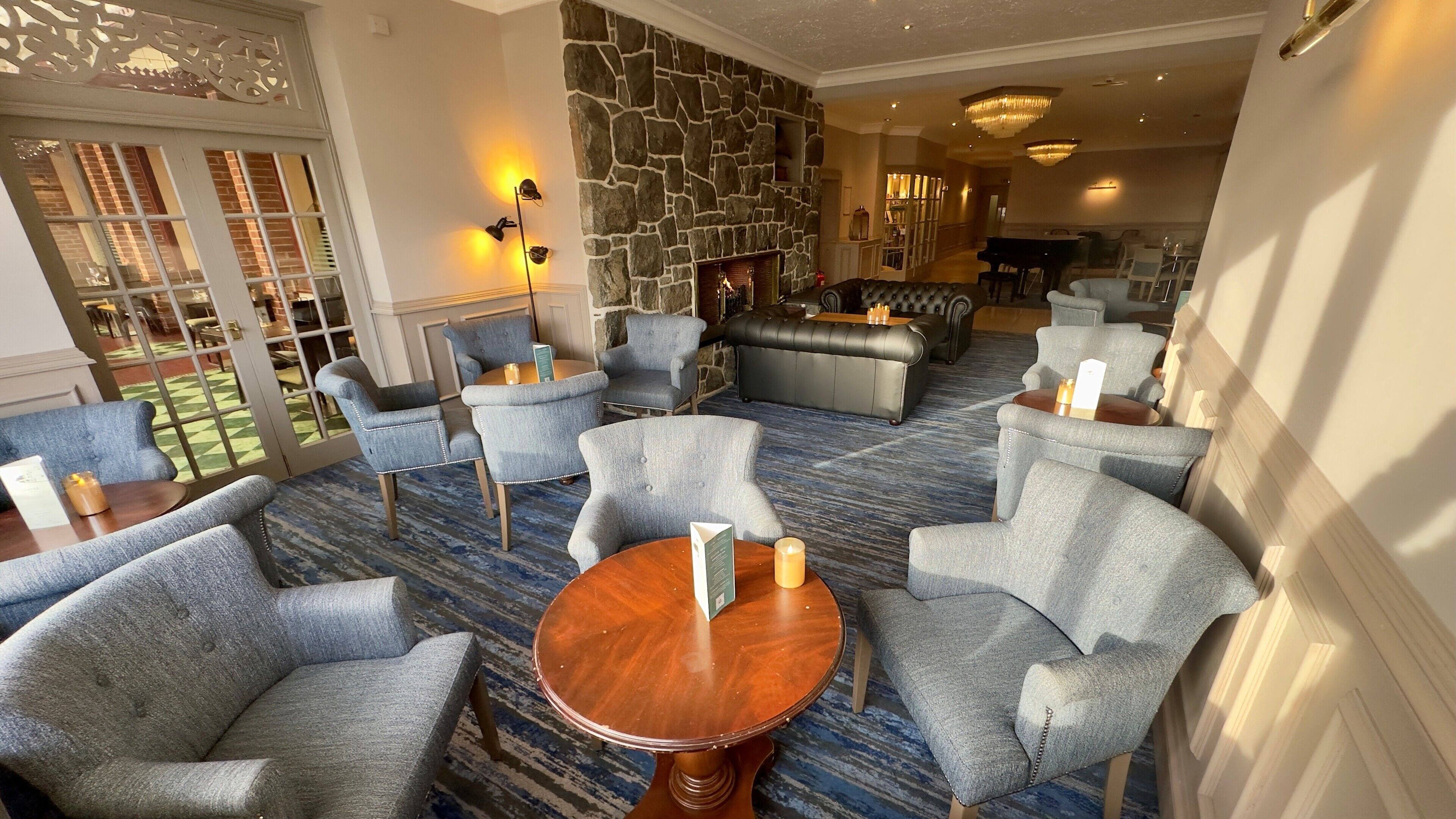 A hotel lobby with grey upholstered chairs, a wooden coffee table, a stone wall, and a fireplace.
