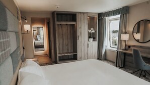 A hotel room with a large bed, a desk with a chair, a wardrobe, a mirror, and a window with curtains. - The Cabarfeidh Hotel (Stornoway)