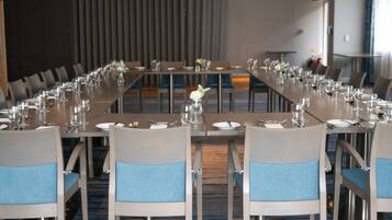 A conference room with long tables set for a meeting, equipped with chairs and table settings.