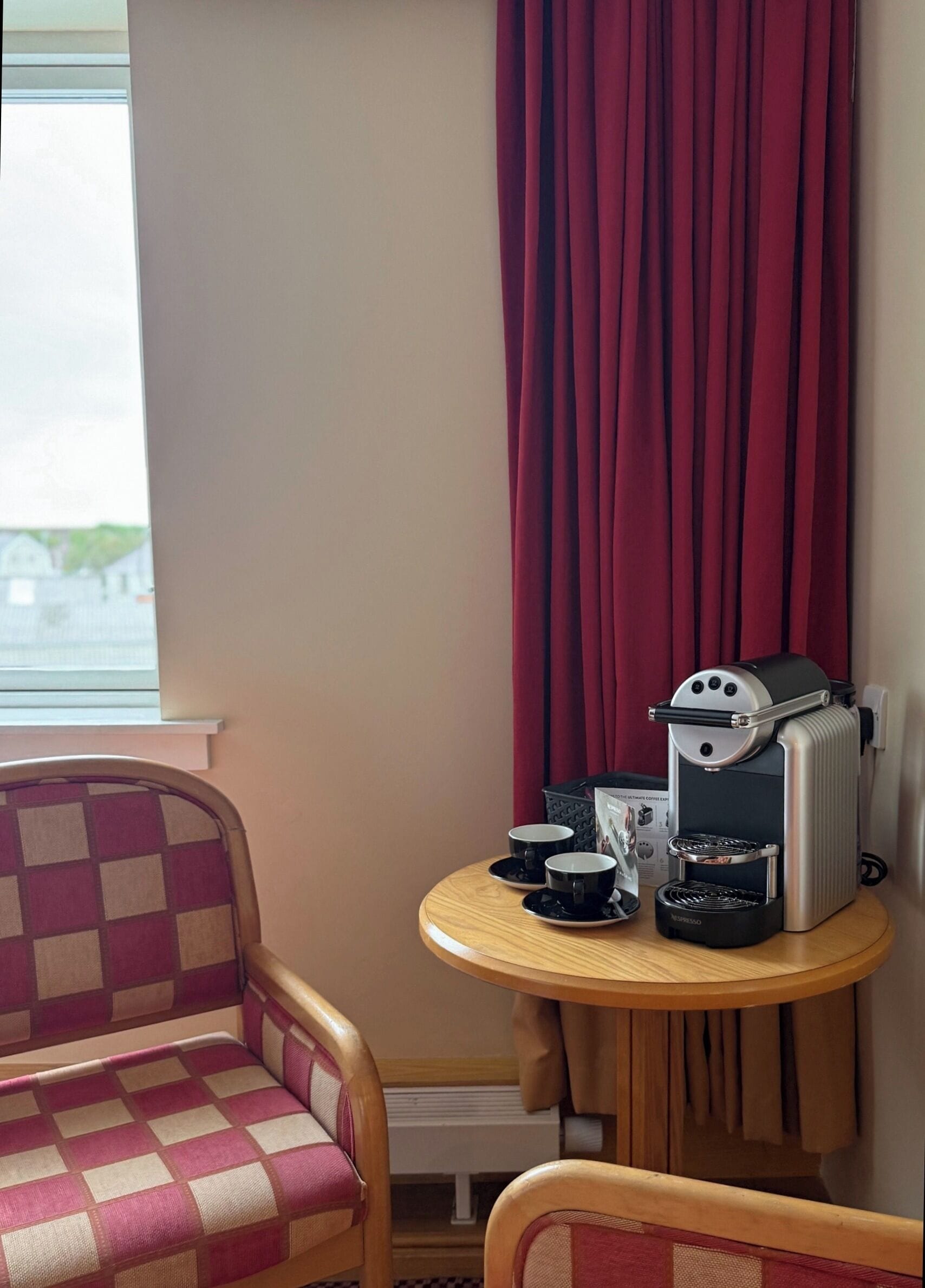 A small room with a checkered sofa, a round wooden table with a coffee machine, cups, and a basket.