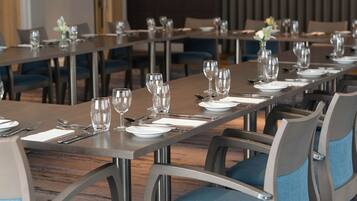 Une salle à manger d’hôtel avec de longues tables dressées pour le service, des chaises dotées de coussins bleus et un sol recouvert de moquette.