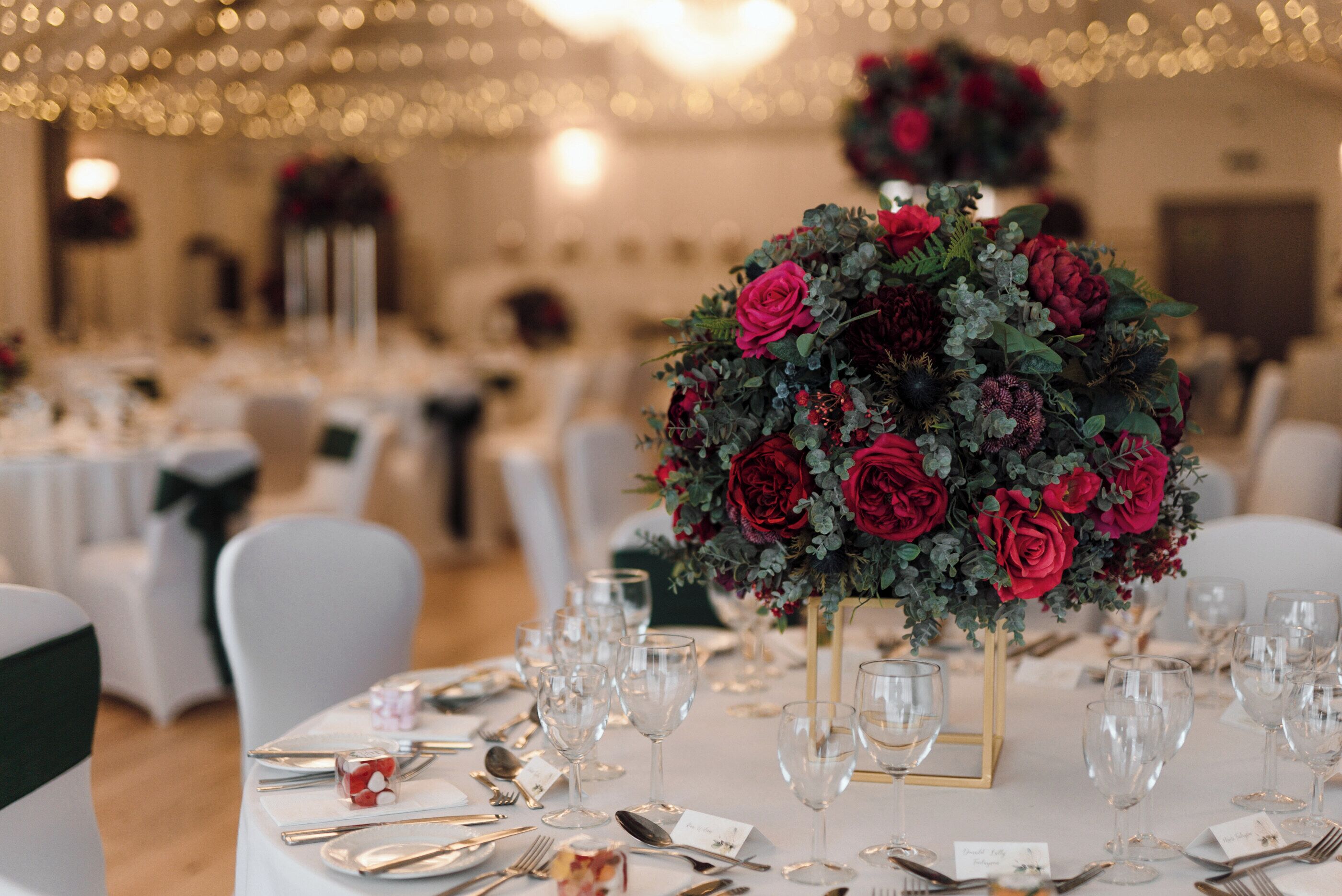 Ein festlich gedeckter Bankettisch für eine formelle Veranstaltung mit einer großen Blumenarragemierung, weißen Tischdecken und ordentlich drapiertem Besteck.