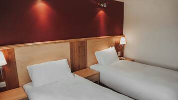 Habitación de hotel con dos camas individuales, cabeceros de madera, lámparas de noche y una pared de acento roja.