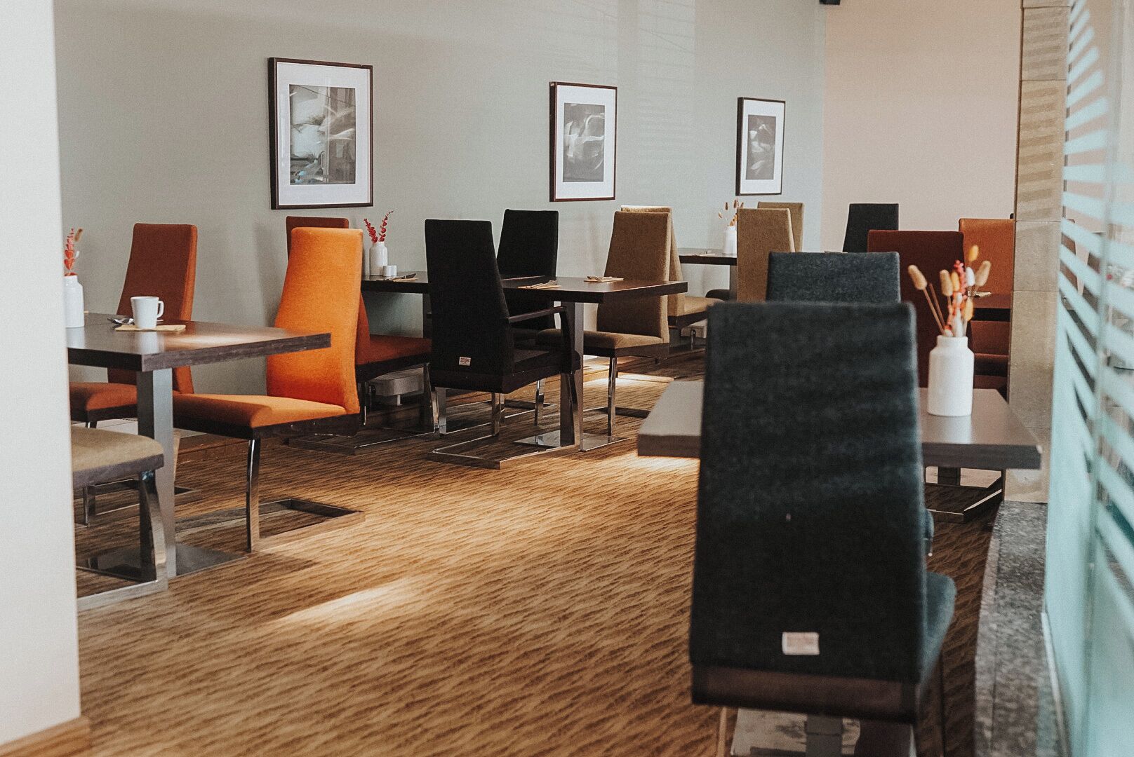A modern dining area with multiple tables and chairs, framed pictures on the walls, and a patterned carpet.