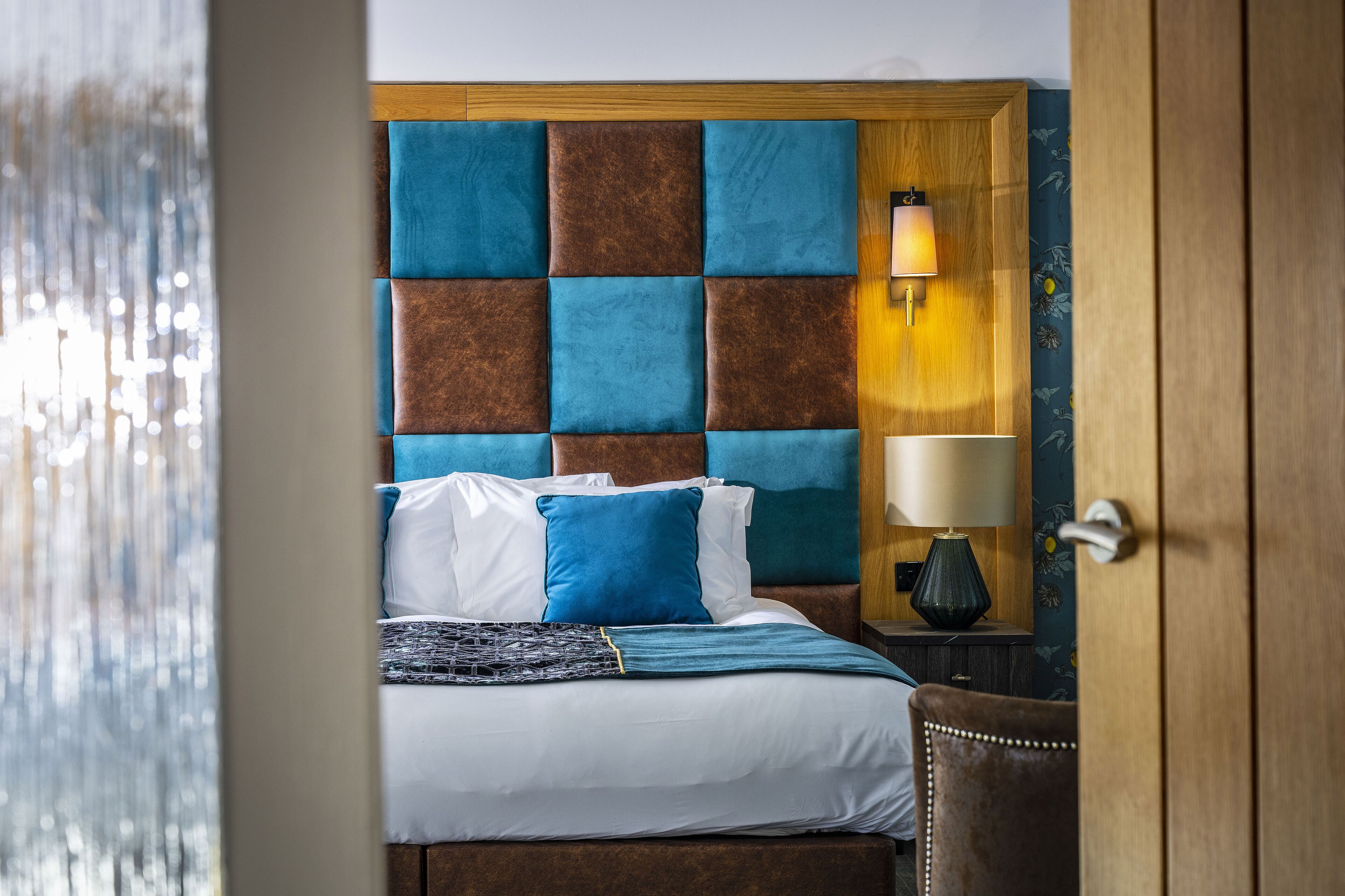 A hotel room with a large bed, a wooden headboard, a bedside lamp, and a nightstand.