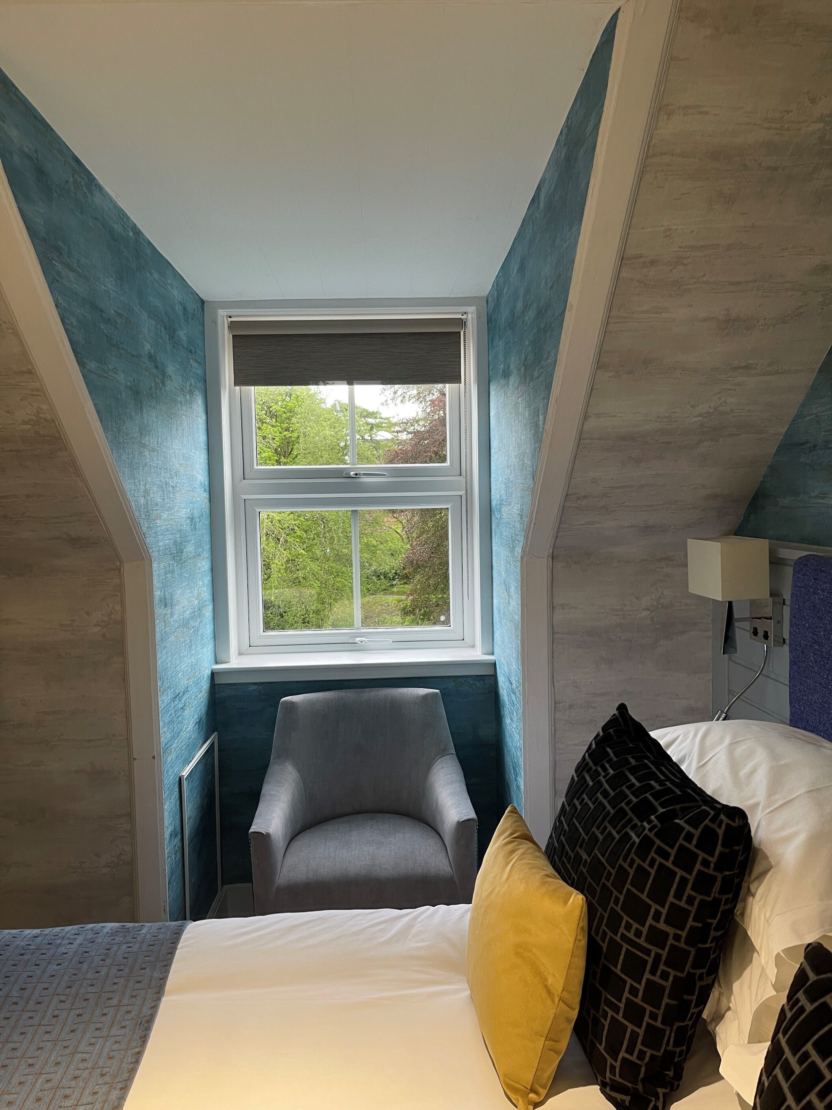 A bedroom with a bed, a chair, a window, and a lamp.