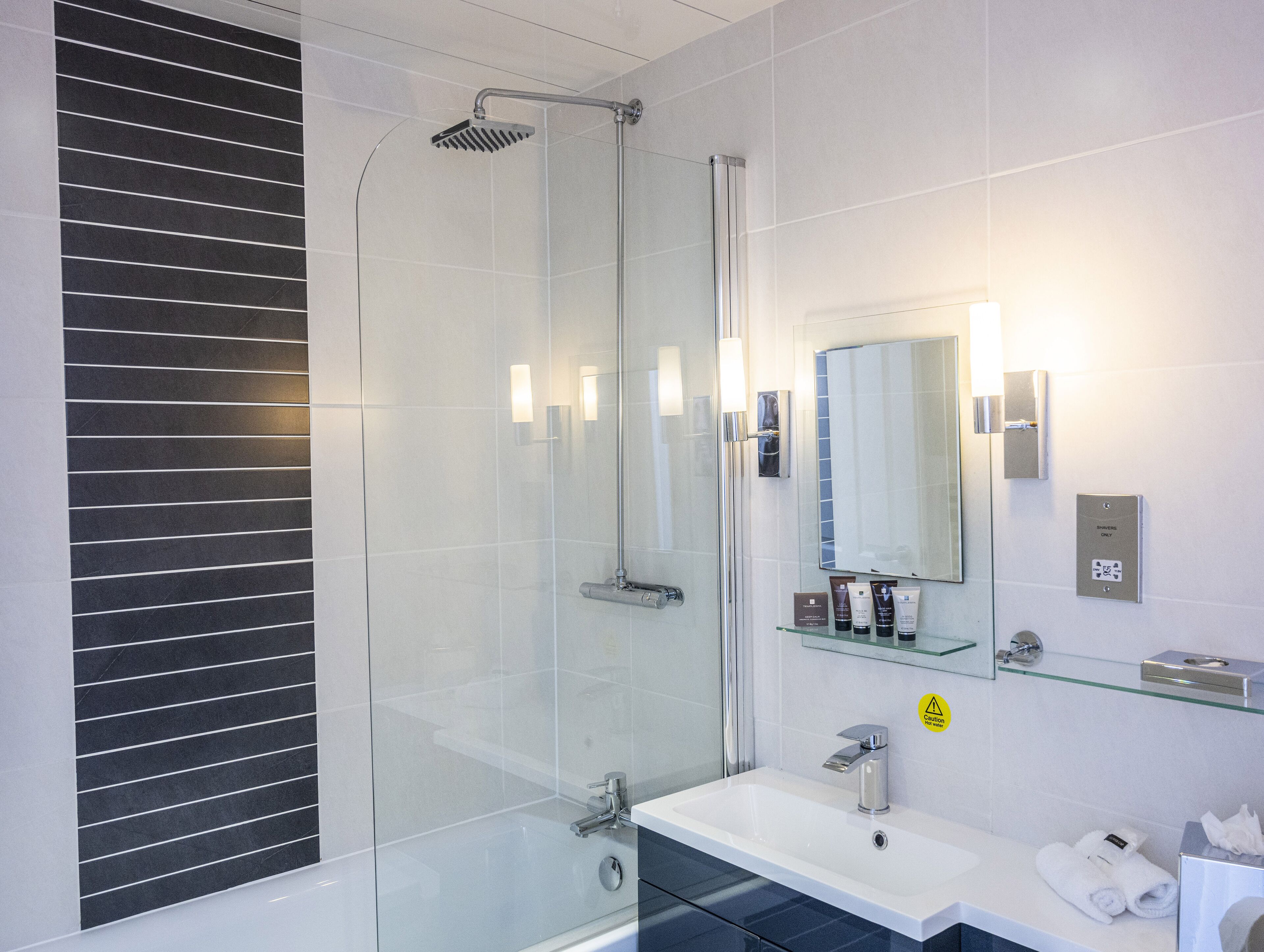 Ein modernes Badezimmer mit Duschkabine aus Glas, einem weißen Waschbecken und einem Spiegel darüber.