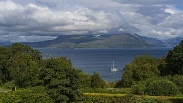 A view of a lake with a sailboat, surrounded by lush greenery and mountains in the background.