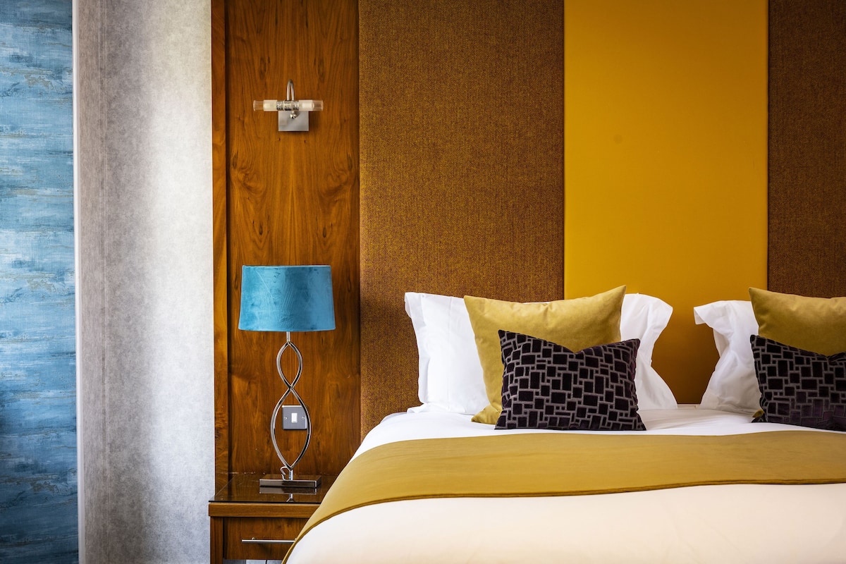 Une chambre d’hôtel avec un grand lit, une tête de lit en bois, une table de chevet avec une lampe et un mur à texture.