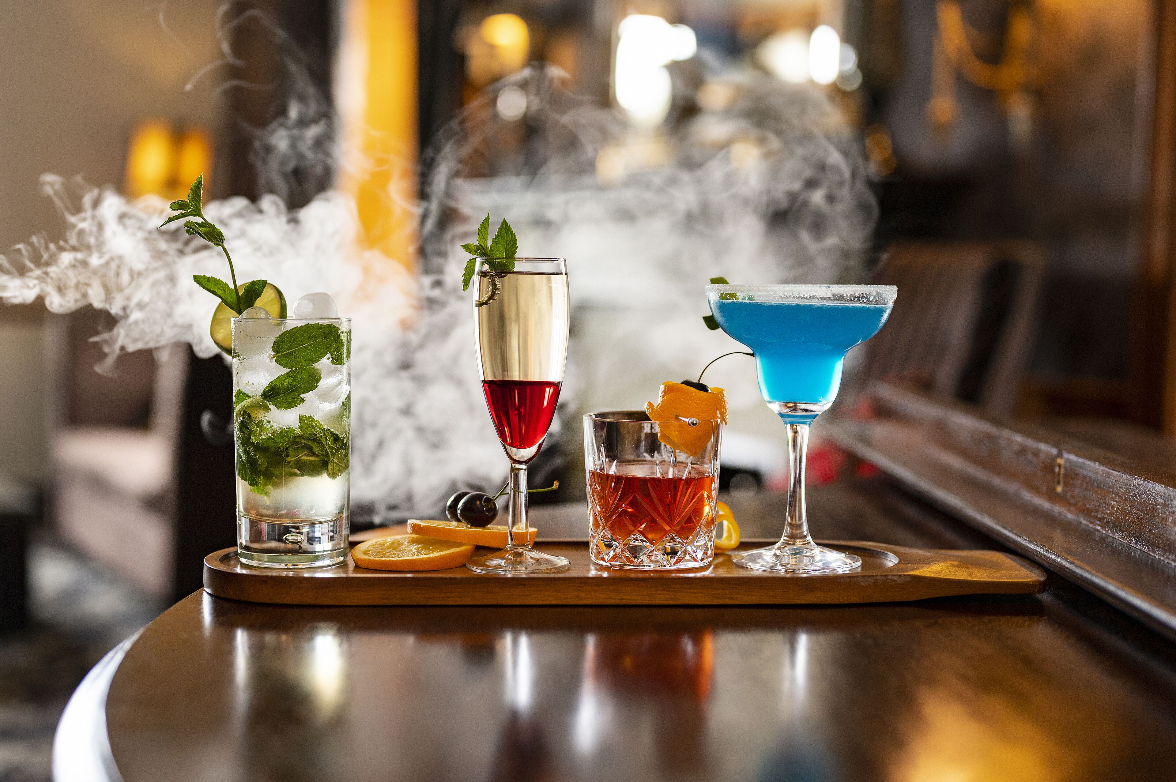 Three cocktails on a wooden tray with a blurred background.