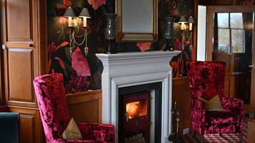 Una habitación con chimenea, dos sillones de terciopelo rojo y papel tapiz con motivos florales.