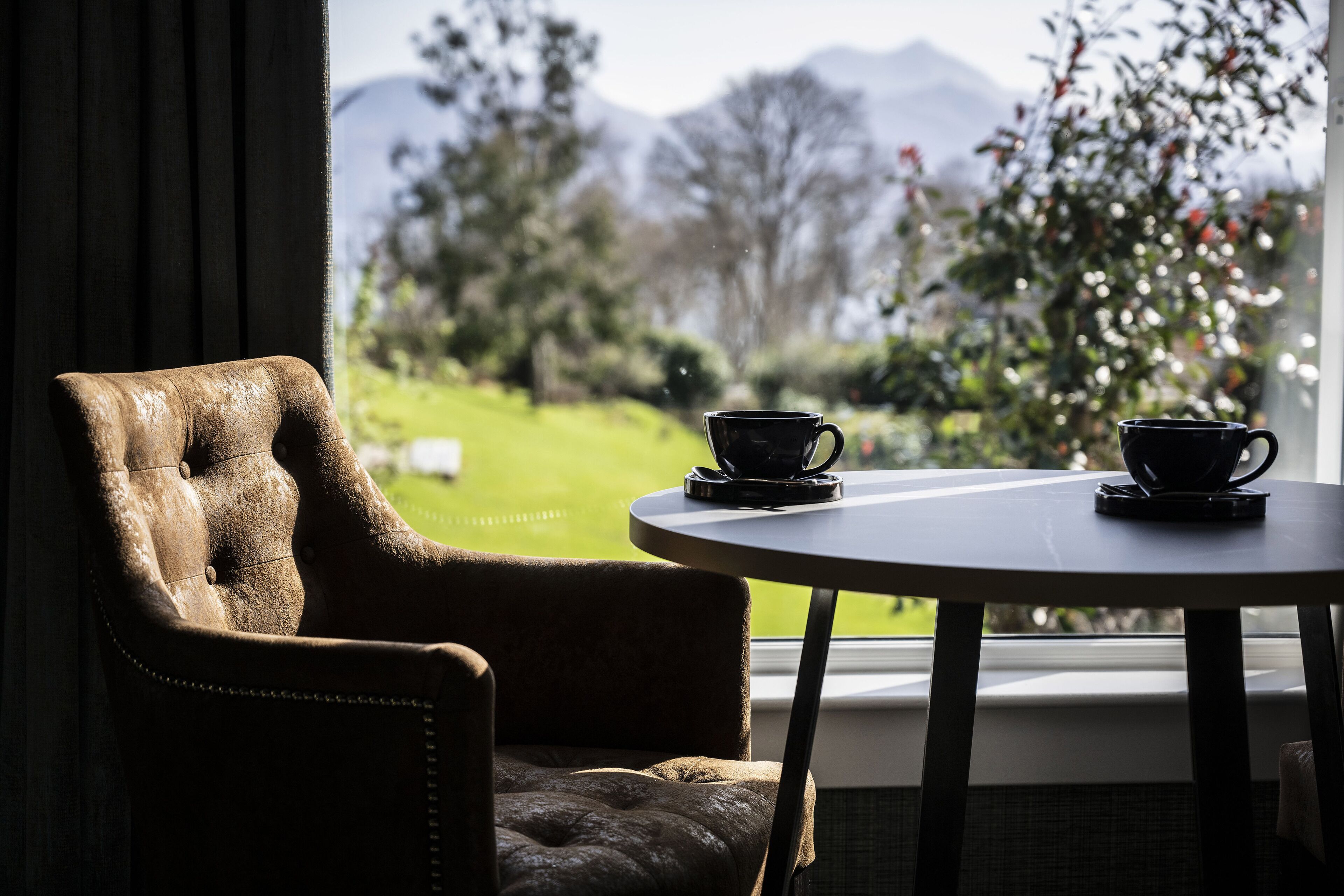 Quarto com vista para montanhas, uma cadeira e duas chávenas sobre uma mesa.