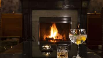 A glass of a clear beverage with a garnish, a candle, and a fireplace in the background.