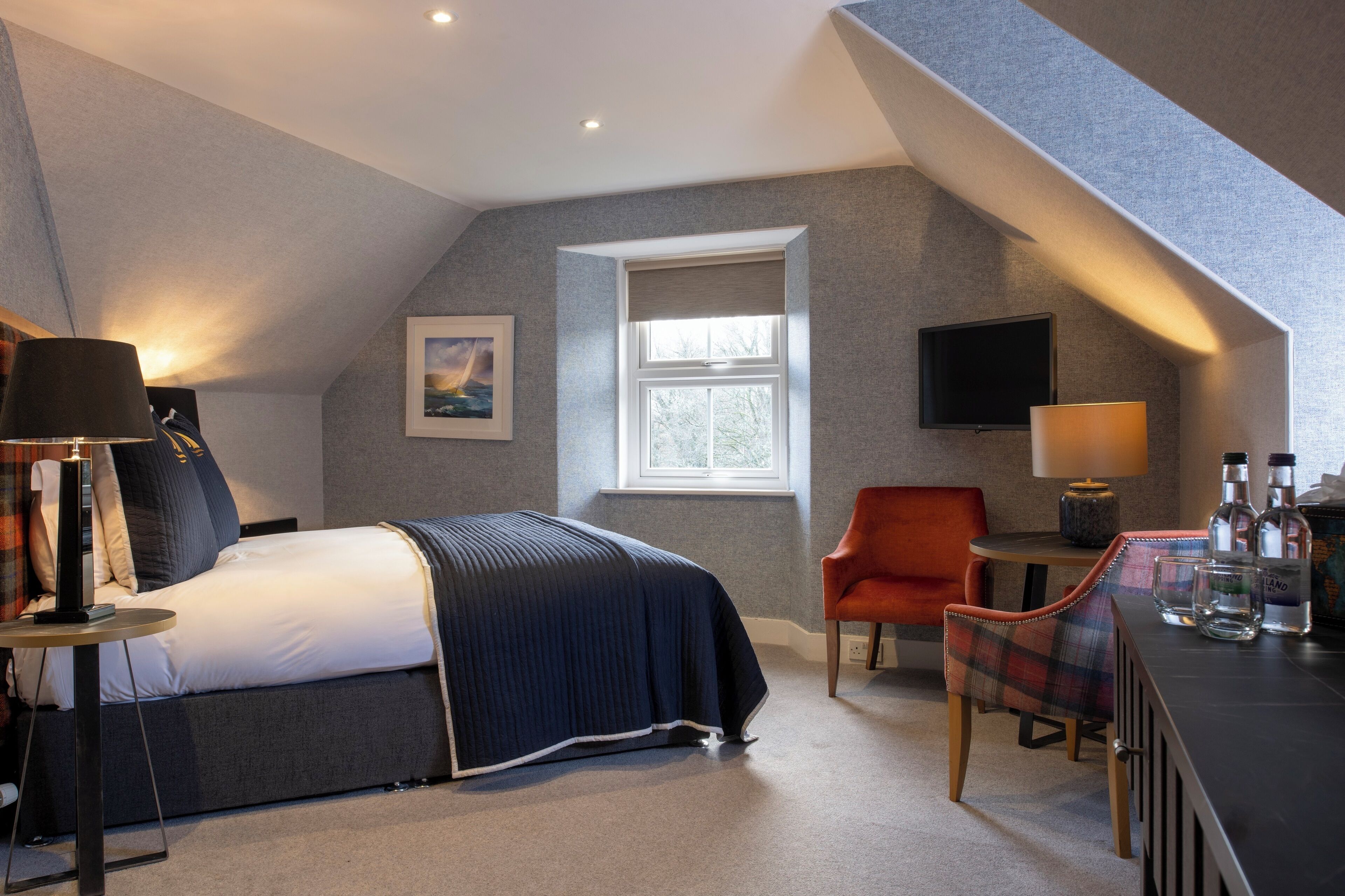 A modern bedroom with a bed, a desk, a chair, a TV, and a window.