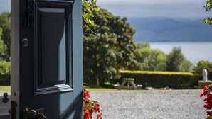 A door with a metal handle and a keyhole, leading to a gravel area with a bench and a statue.