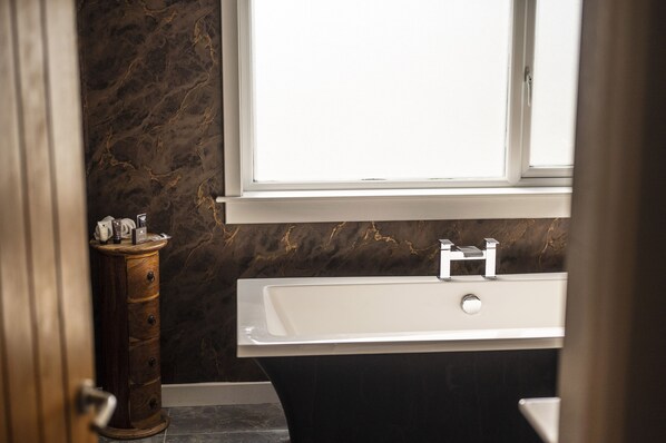 A bathroom with a marble wall, a white sink, and a wooden cabinet.