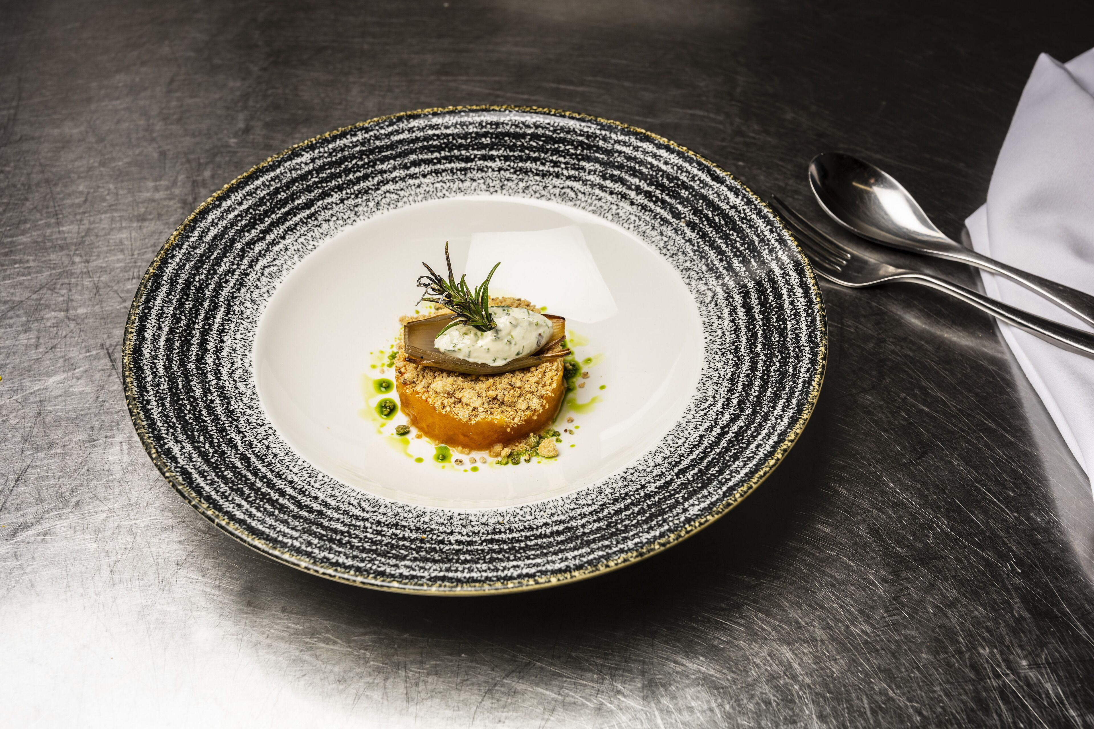 A plate with a dessert on a textured plate, accompanied by a spoon and a napkin on a dark surface.