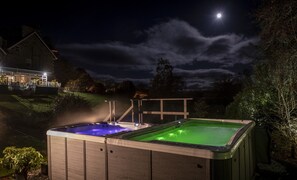Relax in a serene hot tub under the stars, surrounded by a peaceful grassy area and a house in the background.