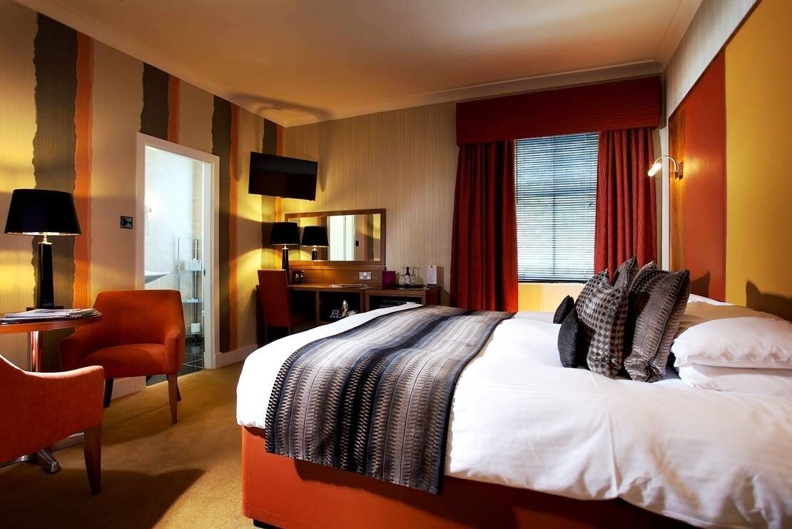Une chambre d’hôtel avec un lit, un bureau, une chaise, une télévision et une fenêtre avec des rideaux.