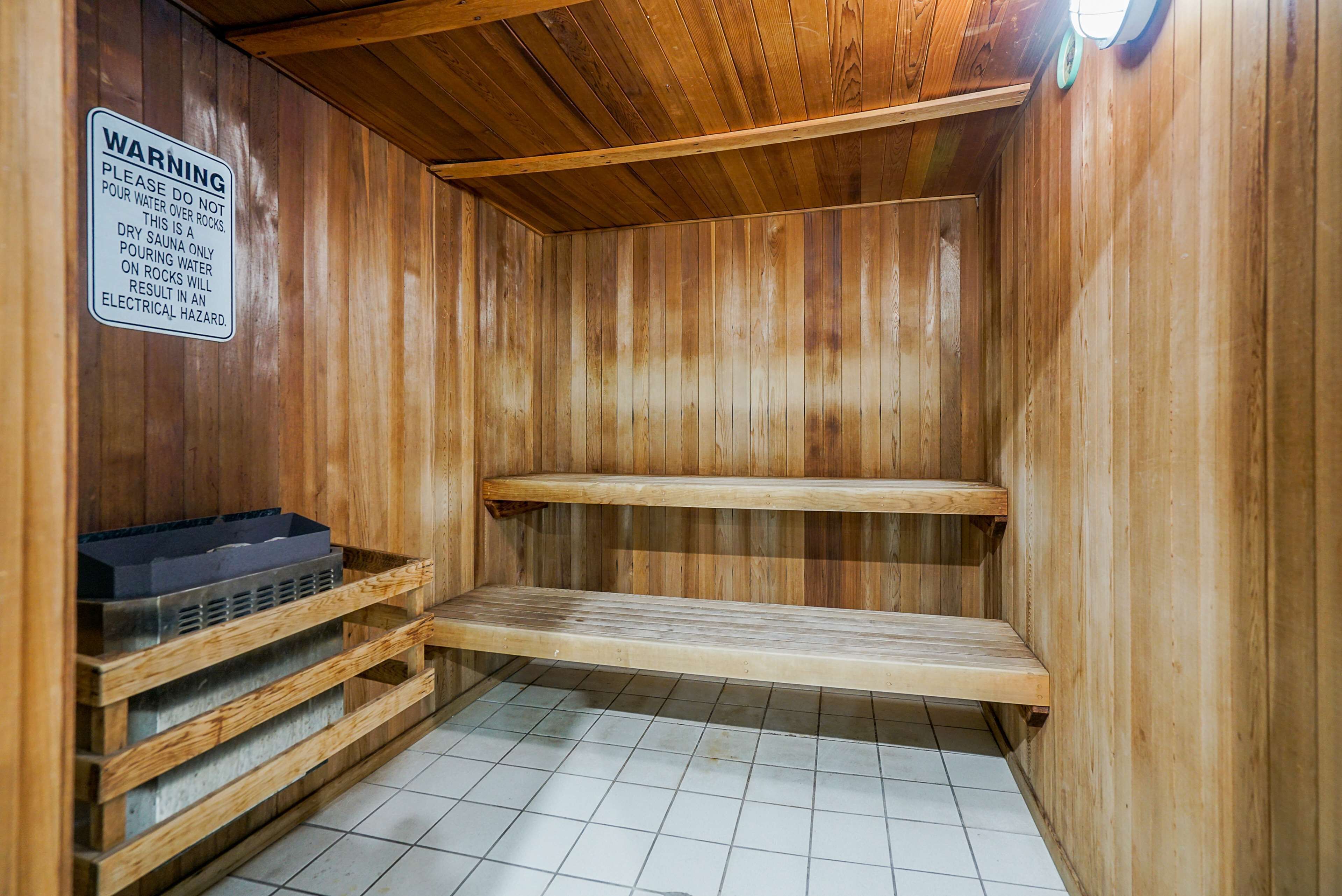 Una sauna con paredes de madera y suelo de baldosas, que incluye un letrero de advertencia sobre seguridad acuática.
