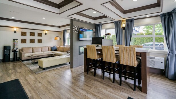 A modern living room with a sofa, a dining table with chairs, a flat-screen TV mounted on the wall, and a large window with curtains.