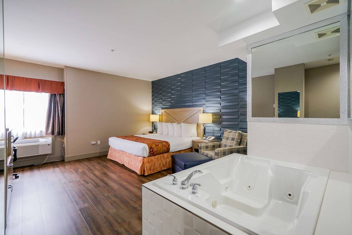 Une chambre d’hôtel avec un grand lit, un canapé séparé, une baignoire et un grand miroir.