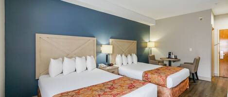 Quarto de hotel com duas camas, uma escrivaninha e uma cadeira.