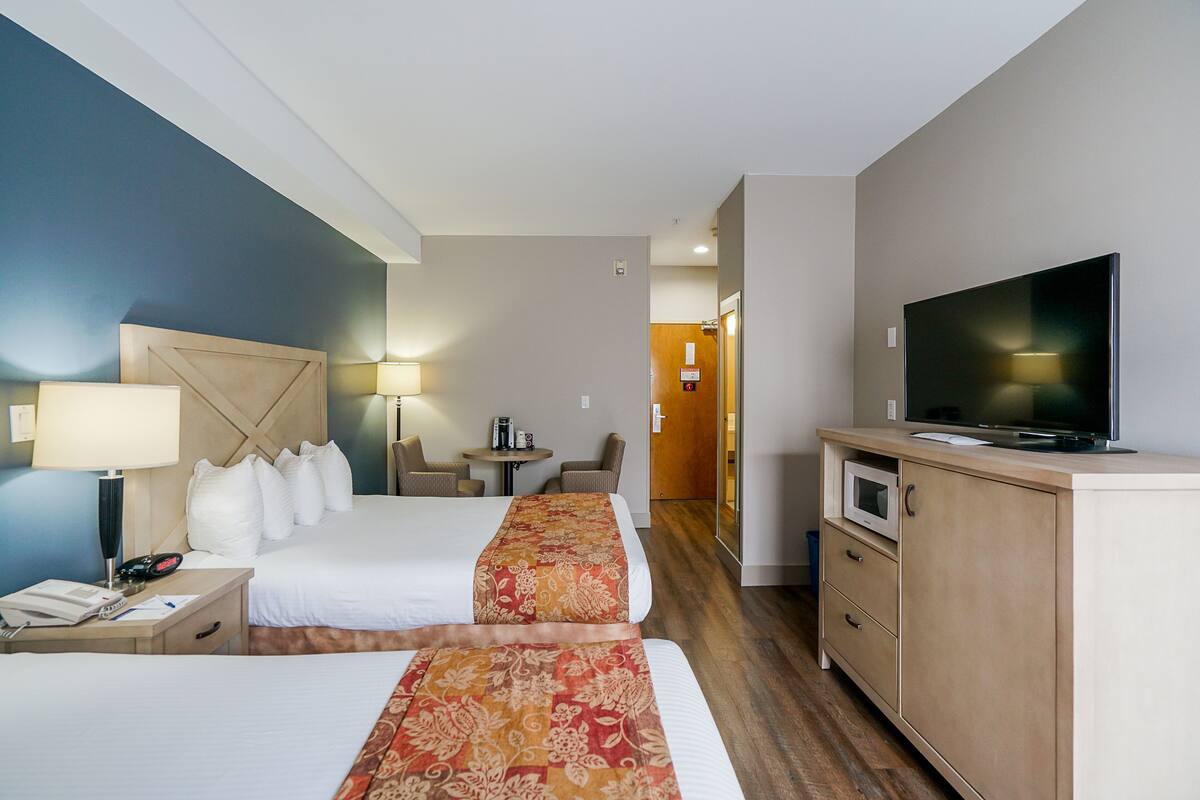 Une chambre d’hôtel avec deux lits, une télévision, un bureau avec une lampe, une petite table avec des chaises et un four à micro-ondes.