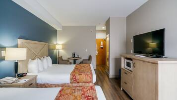 Ett hotellrum med två sängar, en TV, ett skrivbord med en lampa, ett litet bord med stolar och en mikrovågsugn.
