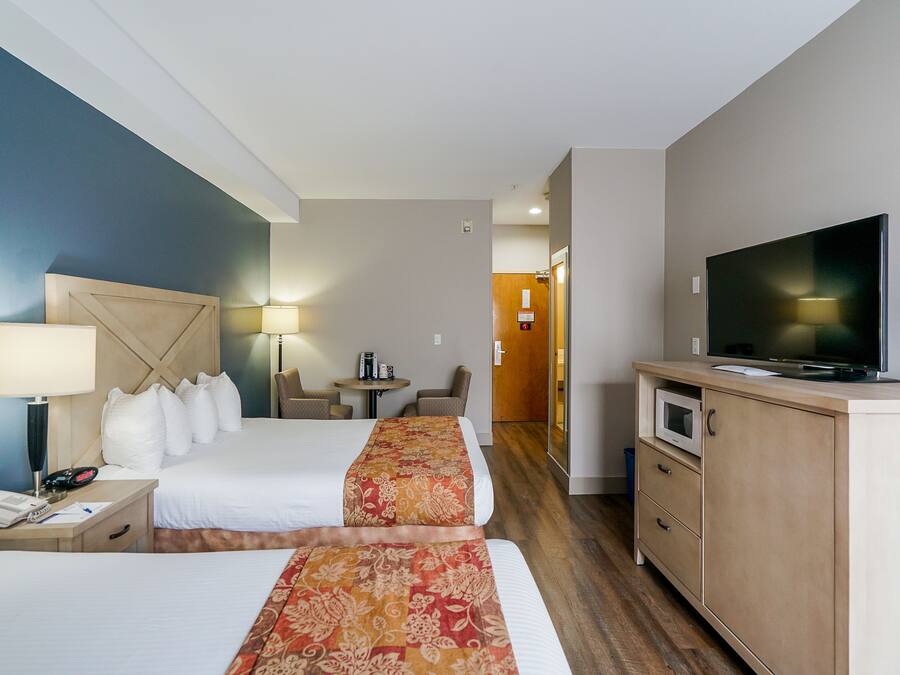 Ett hotellrum med två sängar, en TV, ett skrivbord med en lampa, ett litet bord med stolar och en mikrovågsugn.
