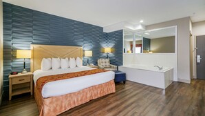A hotel room with a large bed, bedside lamps, a chair, a desk, a mirror, and a bathtub.