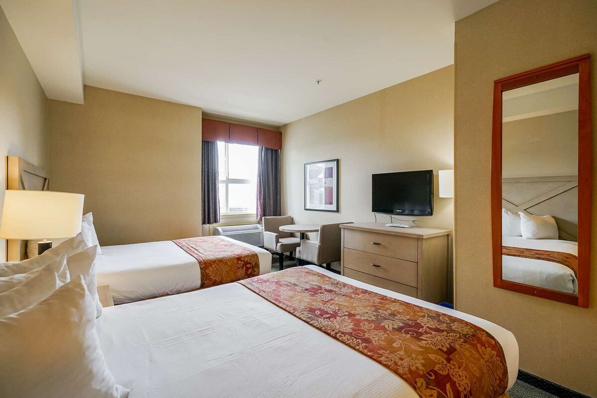 Habitación de hotel con dos camas, un escritorio, una silla, un televisor y un espejo grande.