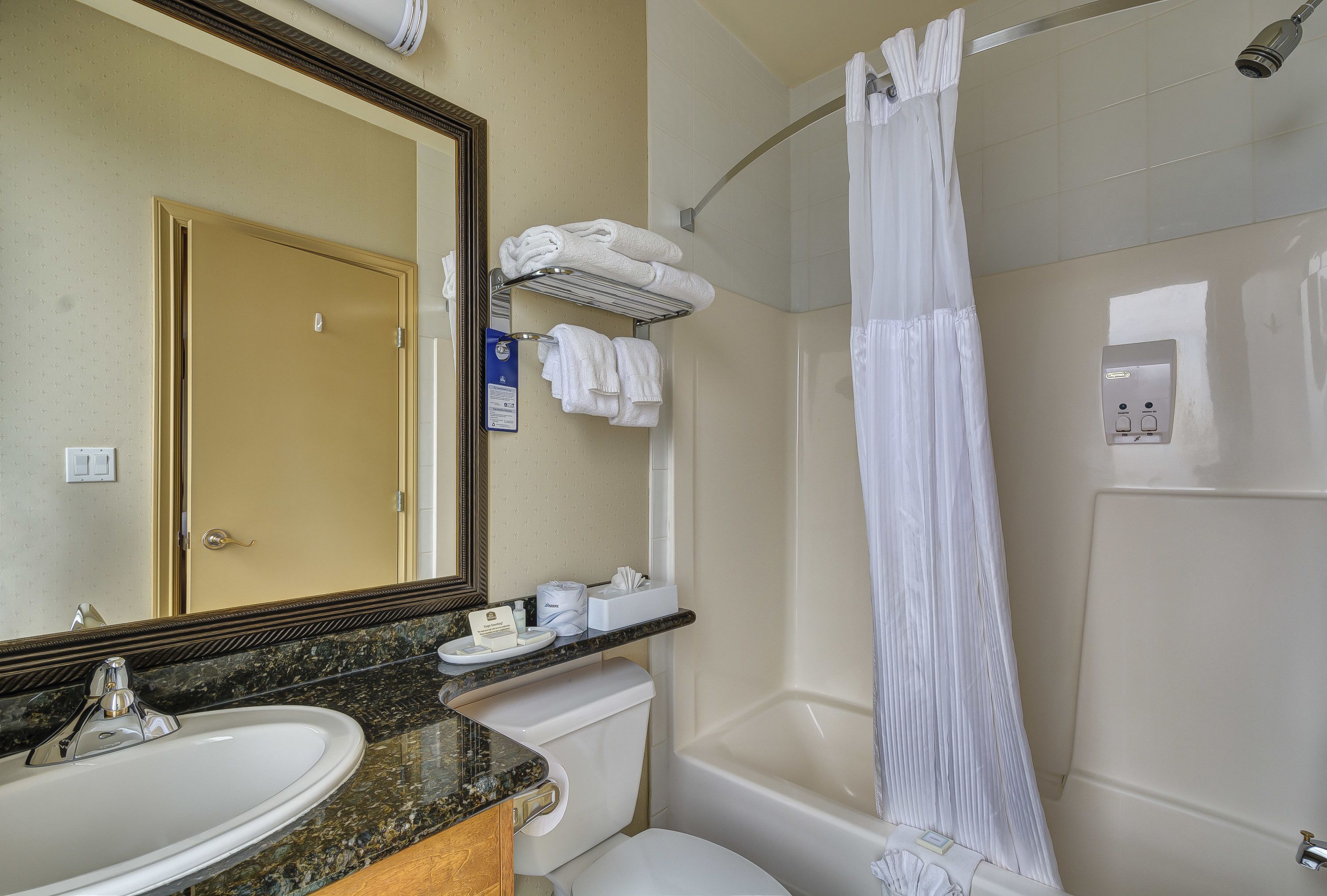 Un baño con lavamanos, inodoro y bañera. Hay un perchero con toallas y una cortina de ducha.
