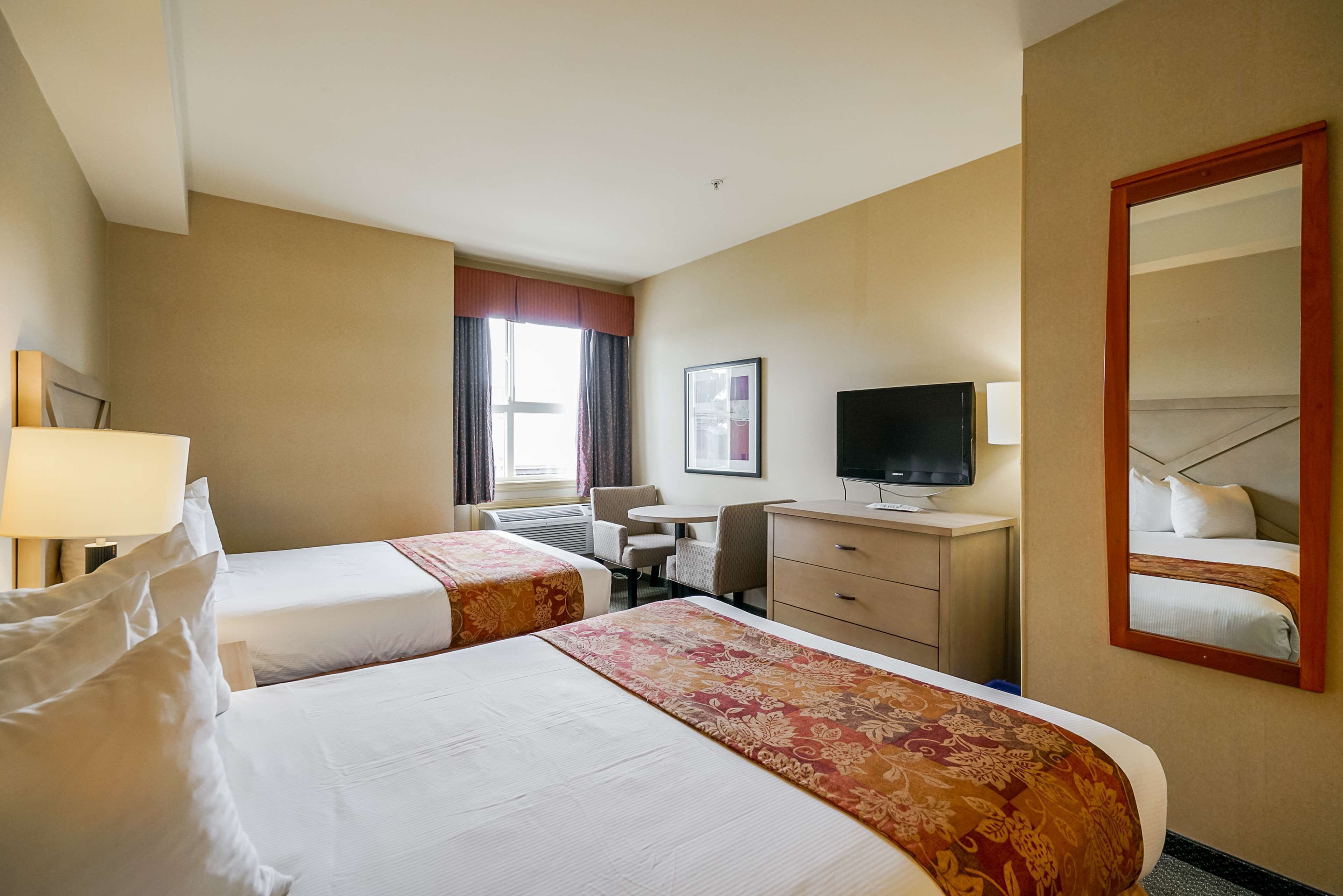 Une chambre d’hôtel avec deux lits, un bureau, une chaise, une télévision et un miroir.