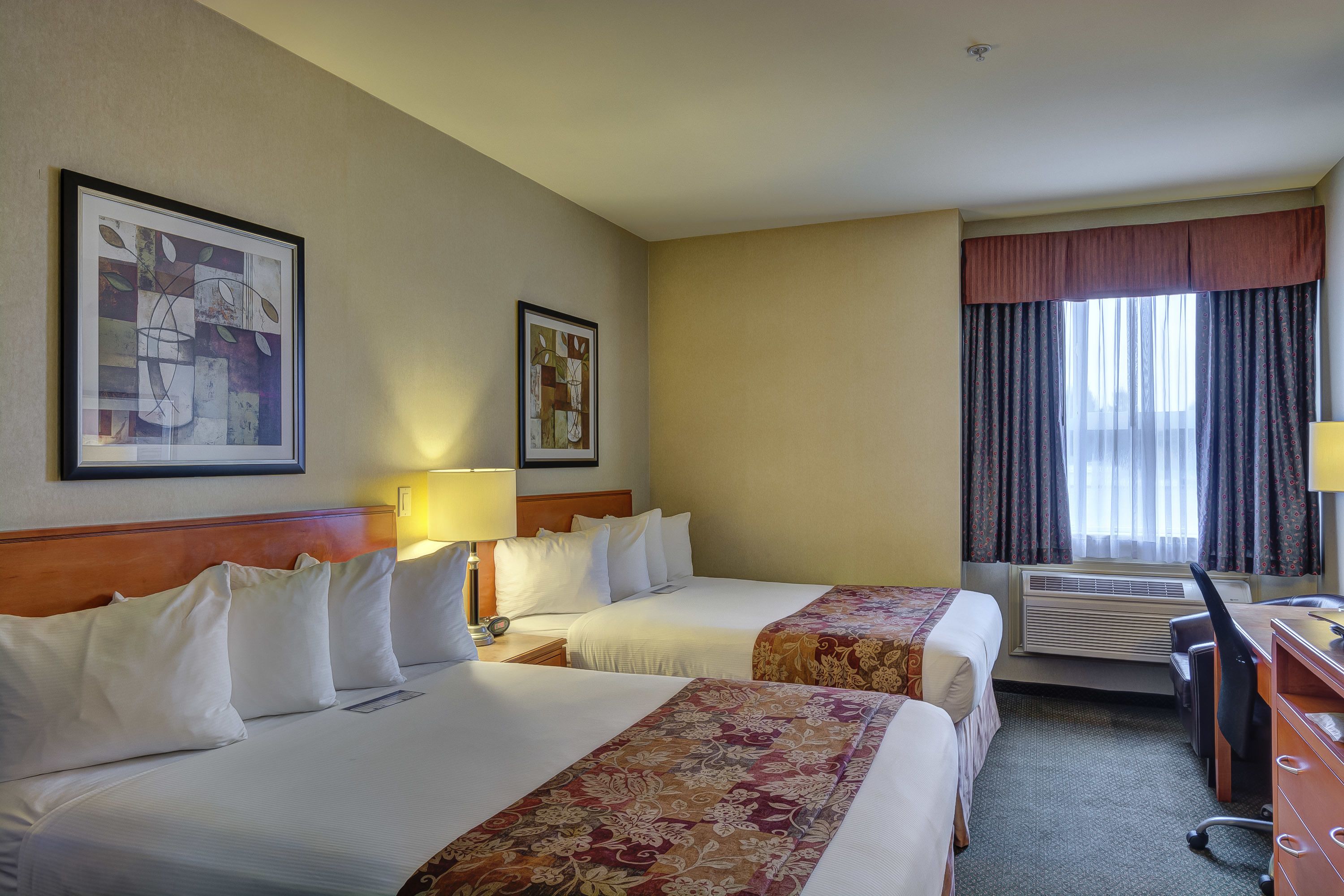 Habitación de hotel con dos camas, un escritorio, una silla y una ventana con cortinas.