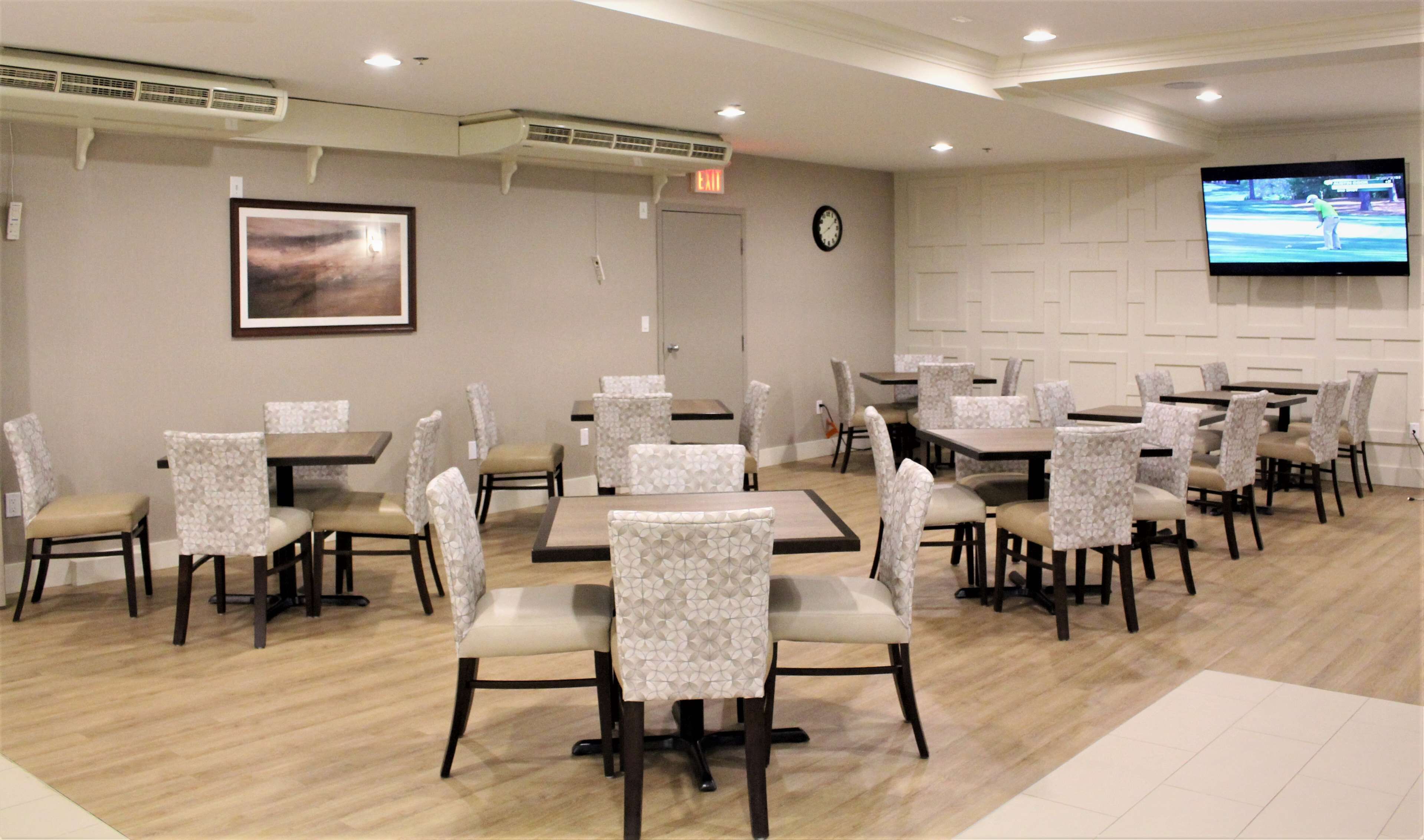 A dining area with multiple tables and chairs, a clock on the wall, and a television screen displaying a golf game.