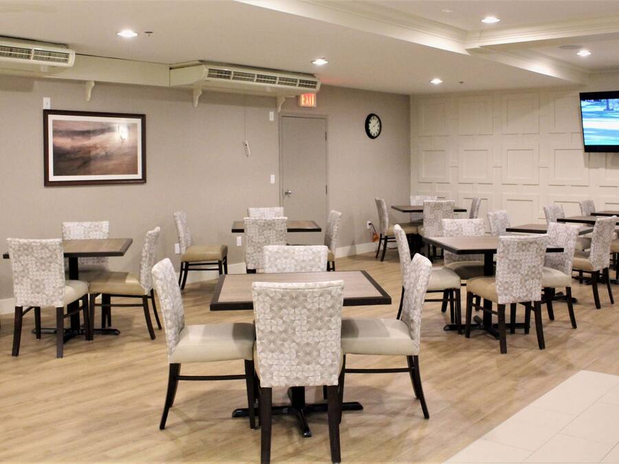 A dining area with multiple tables and chairs, a clock on the wall, and a television screen displaying a golf game.