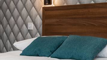 A neatly made bed with teal pillows and a wooden headboard against a diamond-patterned wall.