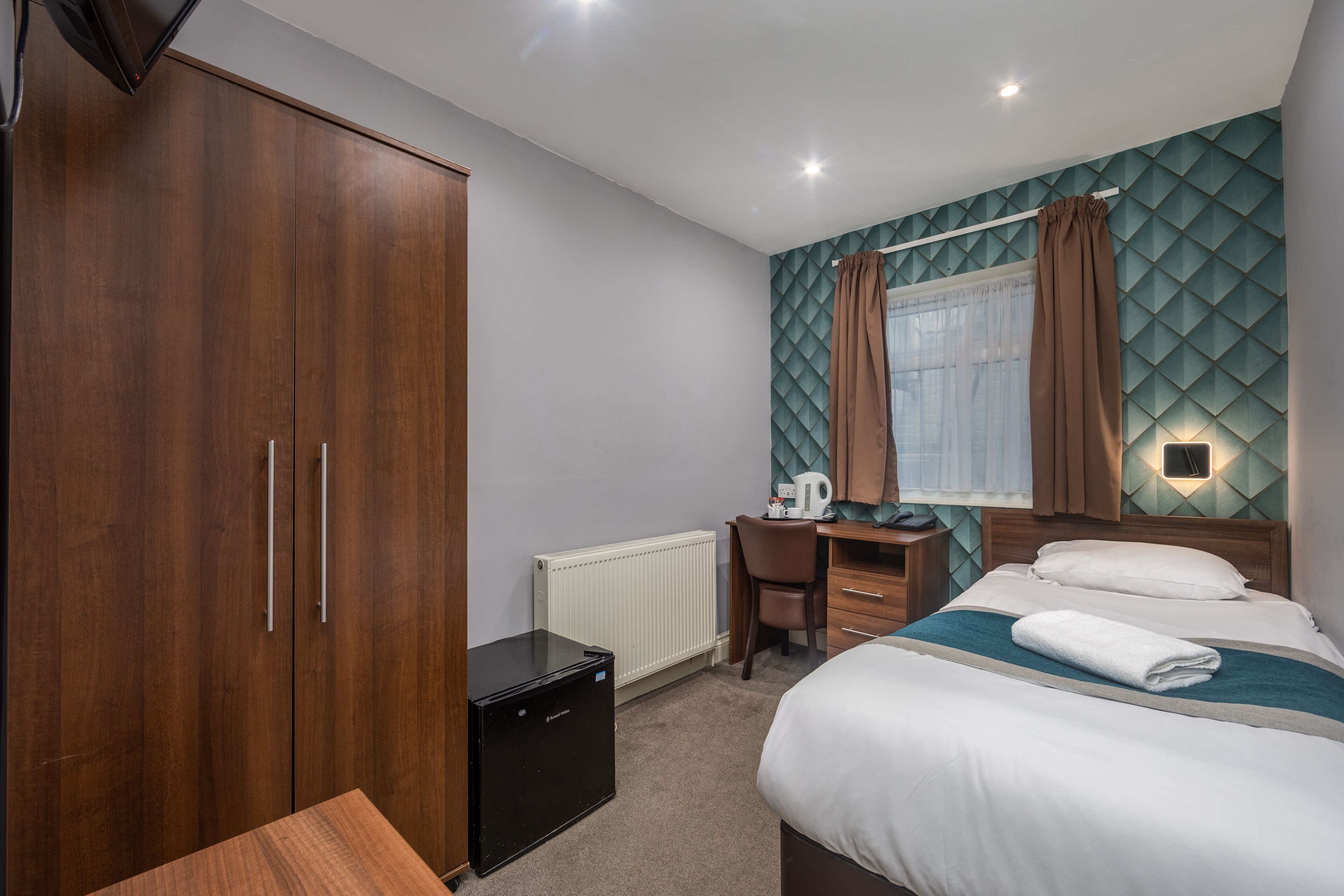 Une chambre d’hôtel avec un lit, un bureau, une armoire et un radiateur.