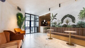 Un hall d’entrée moderne avec un sol en marbre, un canapé marron, une table ronde et une grande plante.