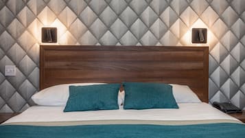 A neatly made bed with a wooden headboard, two teal pillows, and a white pillow. There are two bedside lamps and a black telephone on the nightstand.