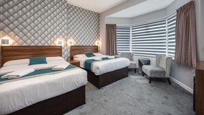 Une chambre d’hôtel avec deux lits, un coin salon et une grande fenêtre avec des stores.