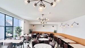 Un espace de restauration moderne avec des tables rondes, des chaises sombres et un lustre original.