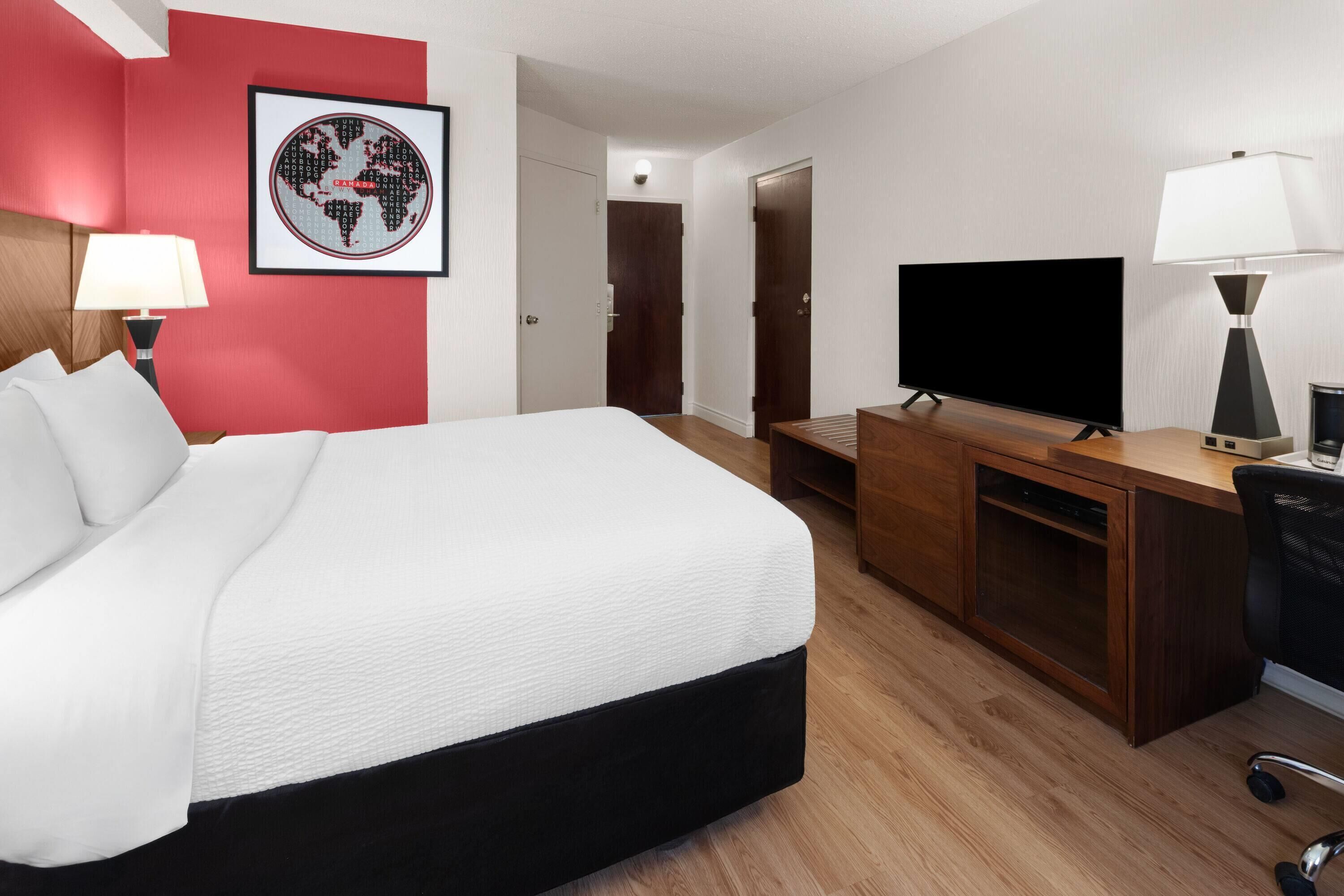 Habitación de hotel con cama, escritorio con televisor, lámpara y un cuadro en la pared.