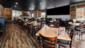 Un restaurante con suelo de madera, varias mesas y sillas, una motocicleta en exhibición y un amplio ventanal.