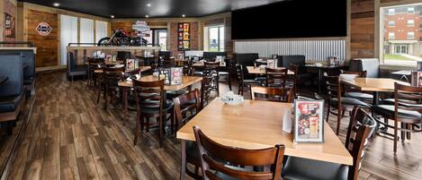 Un restaurante con suelo de madera, varias mesas y sillas, una motocicleta en exhibición y un amplio ventanal.
