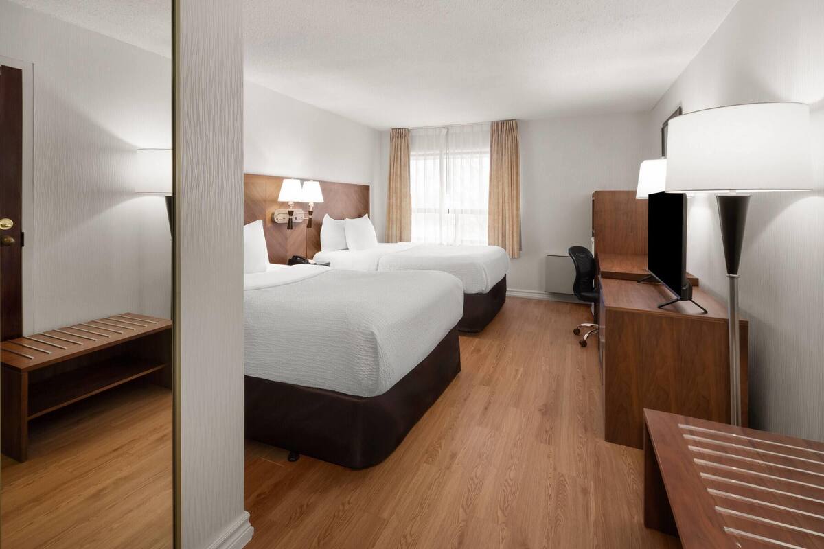 A hotel room with two beds, a desk, a chair, a lamp, and a wardrobe.