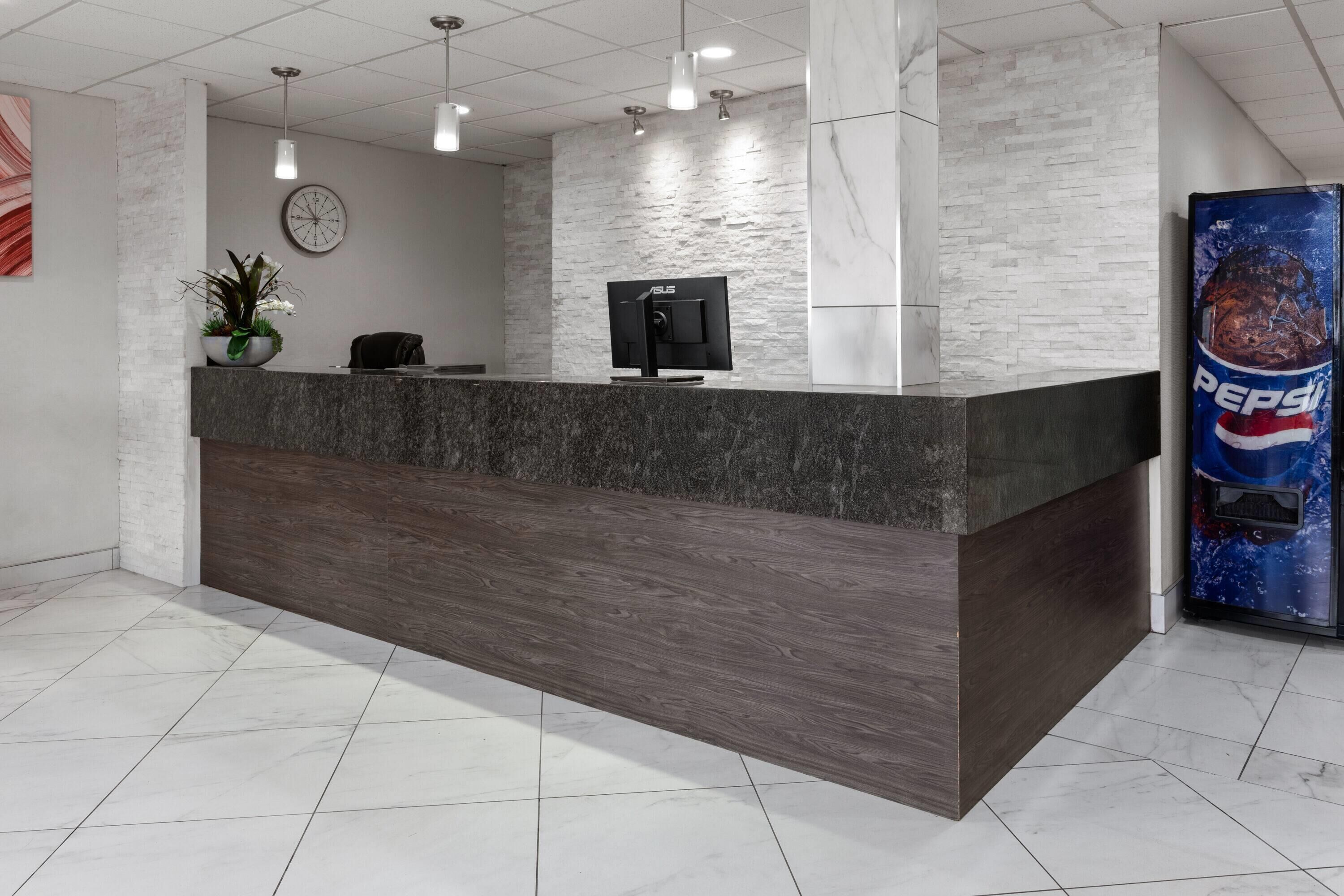 A reception desk with a clock, a computer monitor, and a plant.